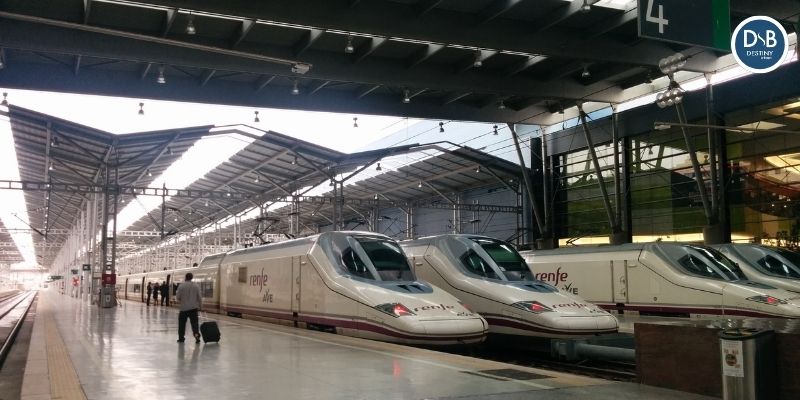 Two white renfe ave high‑speed trains on a sleek platform with a roofed station and a few passengers nearby at platform 4.